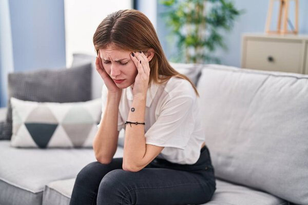 Young blonde woman stressed sitting on sofa at home