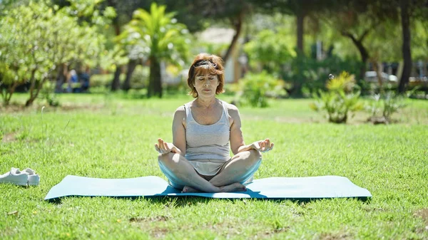 中年妇女坐在公园的地板上练瑜伽 — 图库照片
