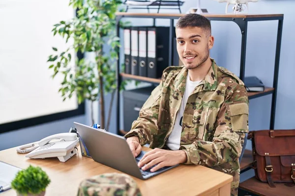 Young hispanic man army soldier using laptop sitting on table at office