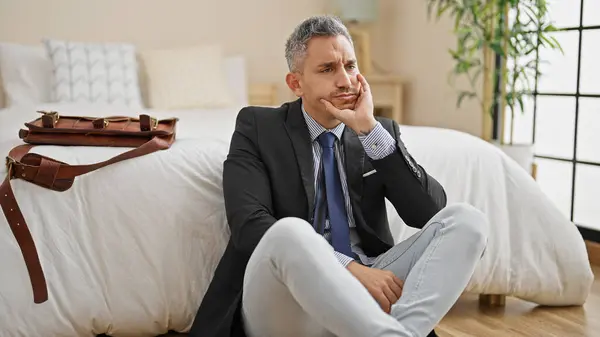 Young hispanic man business worker sitting on floor with serious face at hotel room