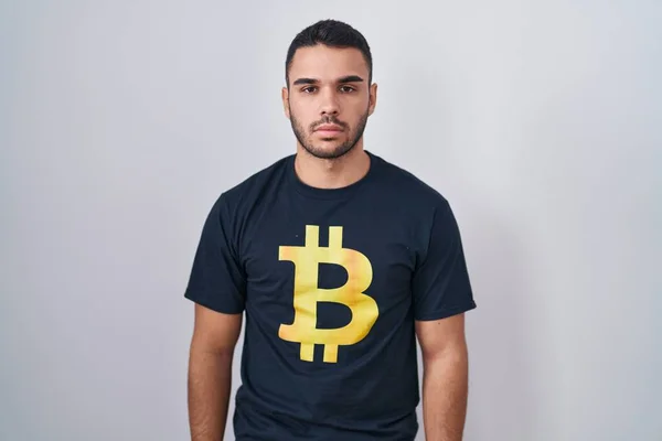 stock image Young hispanic man wearing bitcoin t shirt relaxed with serious expression on face. simple and natural looking at the camera. 