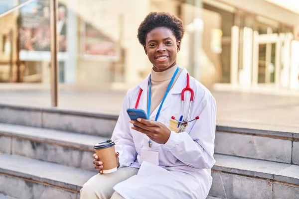 African American Woman Wearing Doctor Uniform Using Smartphone Drinking Coffee — Photo