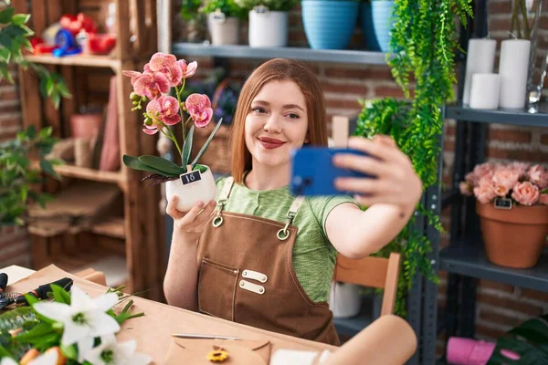 年轻的红头发女花匠在花店里拿着智能手机自拍 — 图库照片