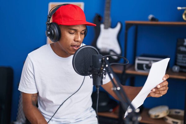 Young latin man artist singing song reading music sheet at music studio
