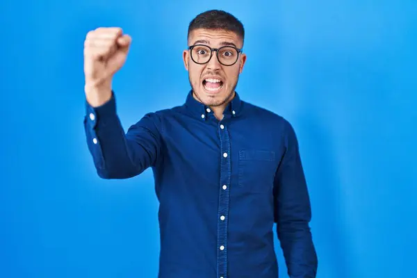 Νεαρός Ισπανός Που Φοράει Γυαλιά Πάνω Από Μπλε Φόντο Θυμωμένος — Φωτογραφία Αρχείου