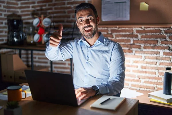 一个西班牙裔男人 留着胡子 晚上在办公室里工作 他赞成用手做一个积极的手势 微笑着竖起大拇指 为成功感到高兴 优胜手势 — 图库照片