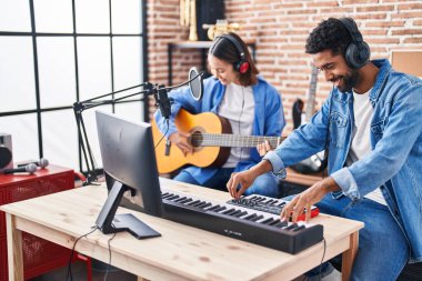 Erkek ve kadın müzisyenler müzik stüdyosunda klasik gitar ve piyano klavyesi çalıyor.