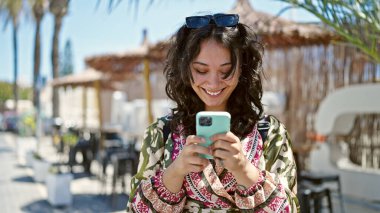 Kafe terasında gülümseyen akıllı telefon kullanan genç, güzel İspanyol kadın.