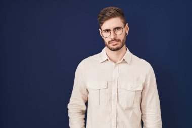 Mavi arka planda duran İspanyol sakallı adam şüpheci ve gergin, sorun yüzünden surat asıyor. negatif kişi. 