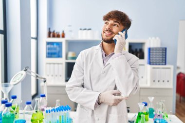 Young arab man scientist smiling confident talking on smartphone at laboratory