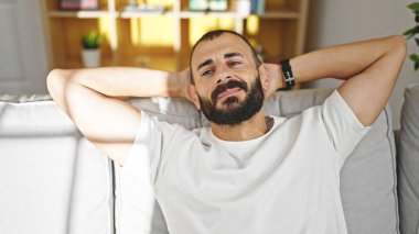 Genç İspanyol adam, ellerini başının üstüne koyup evinde kanepede oturarak rahatladı.