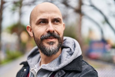 Genç kel adam gülümsüyor. Kendinden emin bir şekilde caddeye bakıyor.