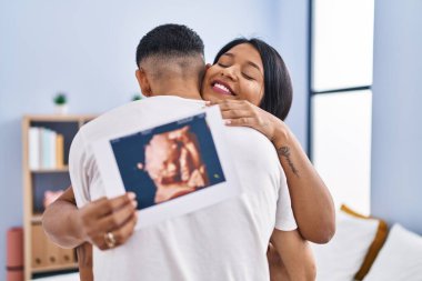 Genç Latin çift bebek bekliyor. Yatak odasında birbirlerine sarılıyorlar.