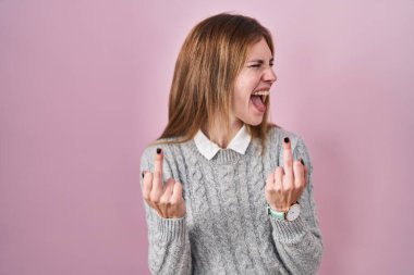 Beautiful woman standing over pink background showing middle finger doing fuck you bad expression, provocation and rude attitude. screaming excited 