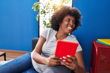 African american woman using touchpad sitting on sofa at home