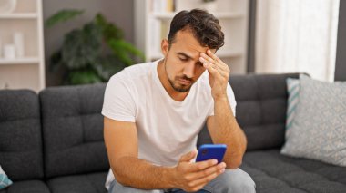 Evdeki kanepede oturan, akıllı telefon kullanan genç bir İspanyol.