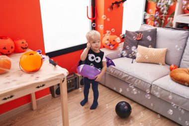 Cadılar Bayramı kostümü giymiş sevimli beyaz çocuk evde sabun köpüğüyle oynuyor.