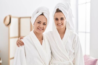 Two women mother and daughter wearing bathrobe hugging each other at bedroom