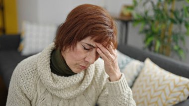 Evde kanepede oturan ve baş ağrısı çeken olgun İspanyol kadın.