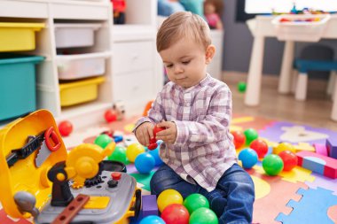 Anaokulunda yerde taşaklarıyla oynayan sevimli beyaz çocuk.