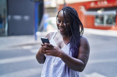 Afro-Amerikalı kadın sokakta akıllı telefon kullanarak kendine güveniyor.