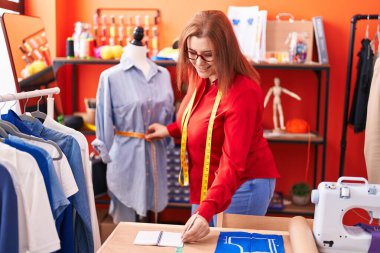 Young beautiful plus size woman tailor measuring dress writing on notebook at atelier