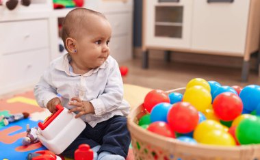 Anaokulunda yerde taşaklarıyla oynayan sevimli beyaz çocuk.