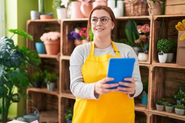 Young beautiful plus size woman florist smiling confident using touchpad at flower shop