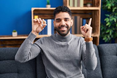 Sakallı İspanyol adam sanal para birimini tutuyor. Bitcoin gülümsüyor. 