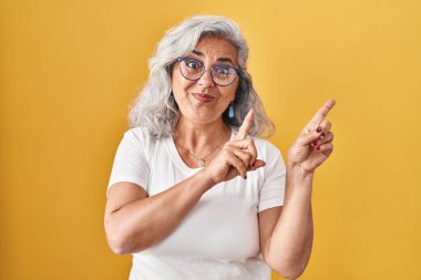 Sarı arka planda gri saçlı orta yaşlı bir kadın gülümsüyor ve kameraya bakıyor.. 