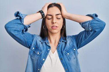 Hispanic woman standing over blue background suffering from headache desperate and stressed because pain and migraine. hands on head. 