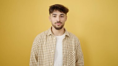 İzole edilmiş sarı arka planda gevşek bir ifadeyle duran genç bir Arap.