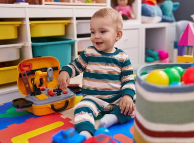 Sevimli beyaz bebek anaokulunda yerde taşaklarıyla oynuyor.