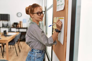 Young caucasian woman business worker writing on cork board at office