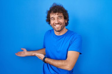 Mavi arka planda duran İspanyol genç adam gülümseyerek doğal bir şekilde içeri girmeye davet ediyor. 