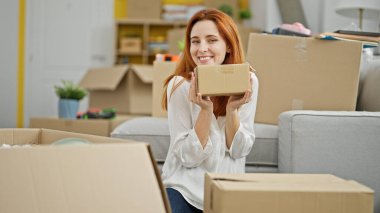 Genç kızıl saçlı kadın yeni evinde kendine güvenen bir paket tutuyor.