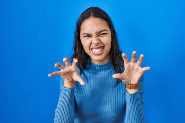 Mavi soyutlanmış arka planda duran Brezilyalı genç bir kadın komik bir şekilde kedi gibi pençe hareketi yapıyor, agresif ve seksi bir ifade. 