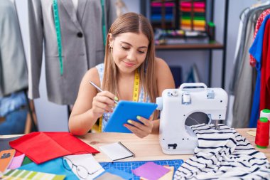 Young beautiful hispanic woman tailor smiling confident drawing on touchpad at tailor shop