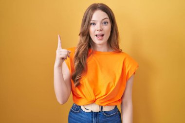 Caucasian woman standing over yellow background pointing finger up with successful idea. exited and happy. number one. 
