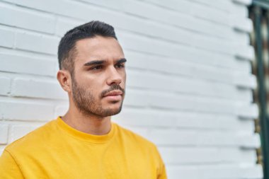 Latin kökenli genç adam ciddi bir ifadeyle sokağa bakıyor.