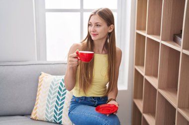 Kafkasyalı bir kadın evdeki kanepede kahve içiyor.