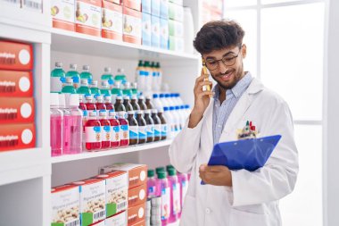 Young arab man pharmacist talking on smartphone reading document at pharmacy