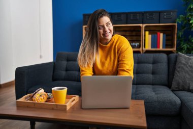 Young beautiful plus size woman having breakfast using laptop at home