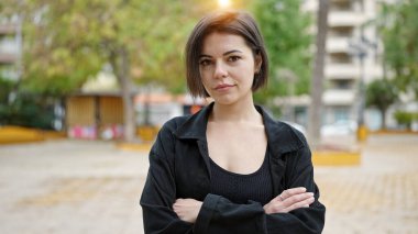 Genç beyaz kadın ciddi bir ifadeyle parkta kollarını kavuşturdu.