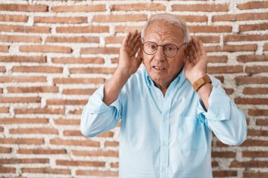 Tuğla duvarın üzerinde dikilen gri saçlı son sınıf öğrencisi iki elini de kulak hareketi yaparken duymaya çalışıyor. Dedikoduya meraklı. İşitme sorunu, sağır 