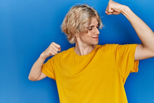 青い背景の上に立っている若い現代人は腕の筋肉を誇りに思って笑っている フィットネスのコンセプト — ストック写真