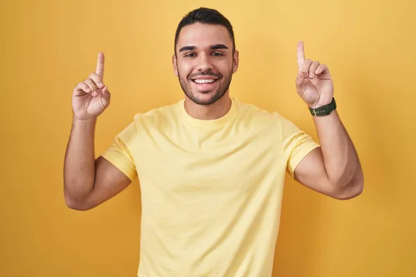 Young Hispanic Man Standing Yellow Background Smiling Amazed Surprised Pointing — ストック写真