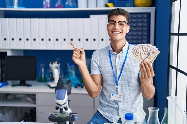 Молодой Латиноамериканец Работающий Научной Лаборатории Держа Руках Доллары Счастливо Показывая — стоковое фото