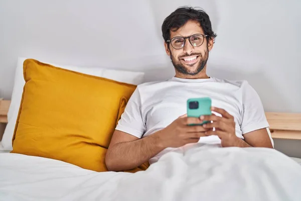 Young Hispanic Man Using Smartphone Sitting Bed Bedroom — Stock Fotó
