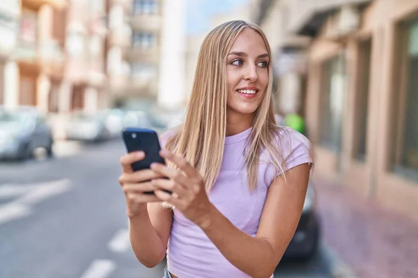 年轻的金发女人在街上用智能手机充满自信地微笑 — 图库照片
